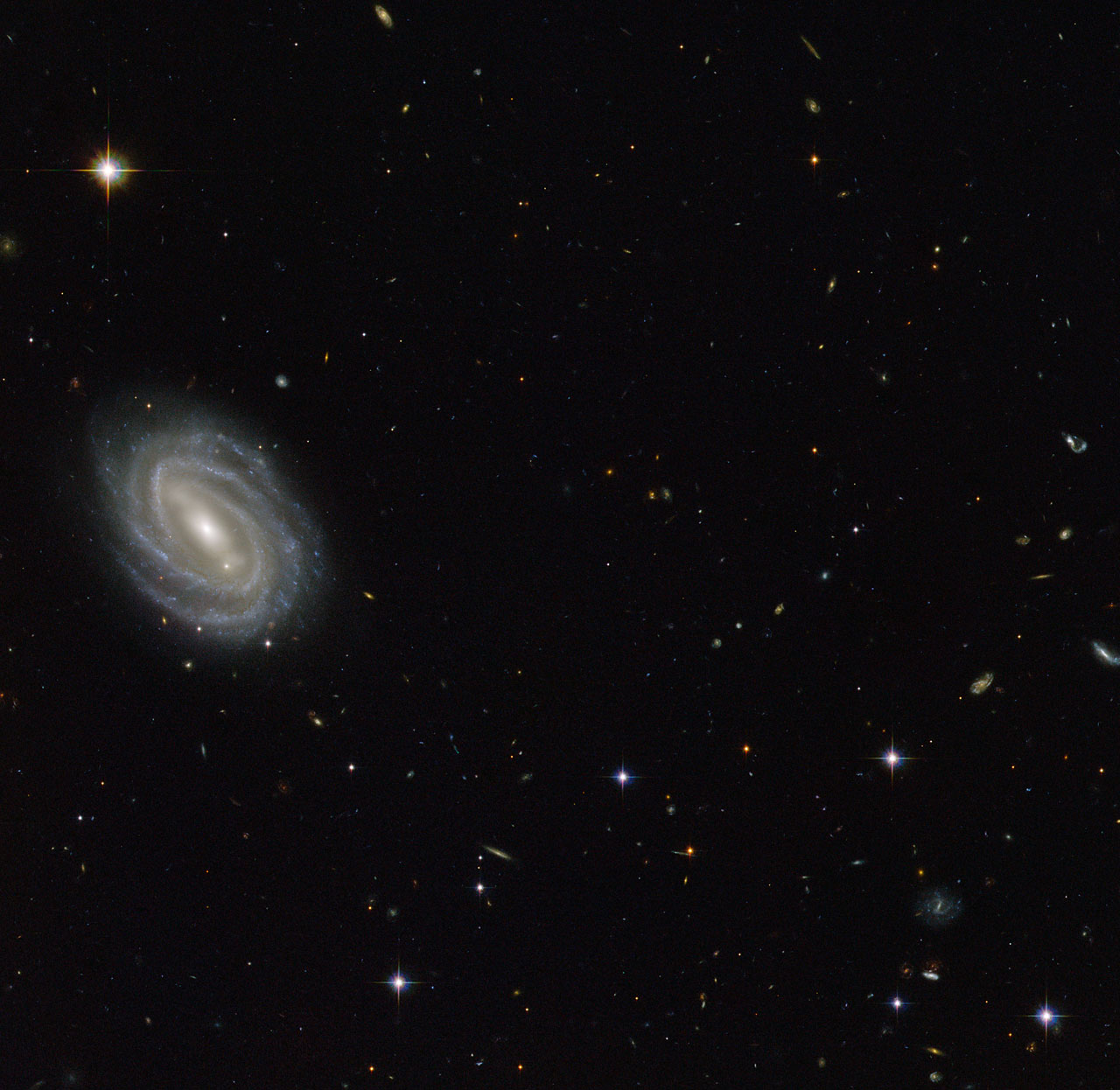 This new NASA/ESA Hubble Space Telescope image shows a beautiful spiral galaxy known as PGC 54493, located in the constellation of Serpens (The Serpent). This galaxy is part of a galaxy cluster that has been studied by astronomers exploring an intriguing phenomenon known as weak gravitational lensing. This effect, caused by the uneven distribution of matter (including dark matter) throughout the Universe, has been explored via surveys such as the Hubble Medium Deep Survey. Dark matter is one of the great mysteries in cosmology. Credit: gsfc/Flickr, CC BY 2.0